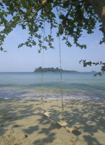 Kai Bae Beach view from sandy beach out towards Koh Man Nai Island with wooden swing in the foreground hanging from trees overhead.