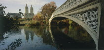 Central Park  Bow Bridge.  View along side of cast iron bridge across lake lined by trees and overlooked by city buildings and the San Remo towers.