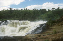 View towards fast flowing water with forest behind.