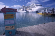 St Johns Harbour.  Wooden jetty in the foreground with painted sign directing visitors to shops and cafes.  Cruise boats in the water behind.