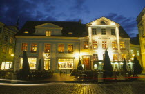 Raekoja Plats.  Exterior of cafe and restaurant and clothes shop illuminated at night.