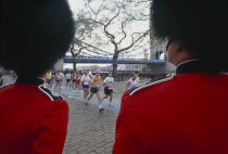Runners and Tower Bridge seen between two Guardsmen both wearing a Busby and red tunicBearskin