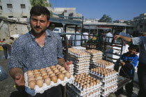Man selling eggs in street market  standing holding tray with more stacked behind him.