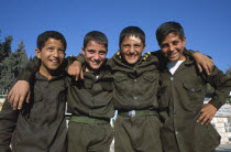 Four smiling schoolboys in uniform  standing in a line with their arms around each others shoulders.  Three quarter view.
