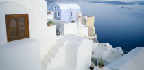 Oia.  White painted terrace and roof tops overlooking sea with distant ferry and coastline behind.