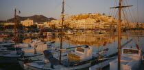 Hora.  View over moored boats and harbour towards town reflected in the water in evening light.