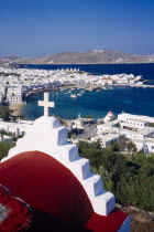 View over Mykonos town and harbour.  Part view of church roof in the foreground.