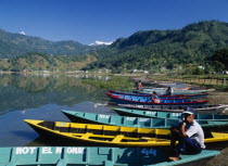 Painted wooden rowing boats on Lake Phewa with tree covered hillside behind.
