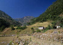 White painted buildings on lower slopes of terraced hillside with tree covered hills behind and distant mountains.