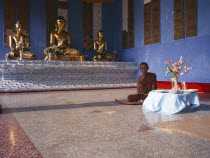 Shwedagon Pagoda interior.  Monk sitting beside a raised altar with three seated  golden Buddha figures.