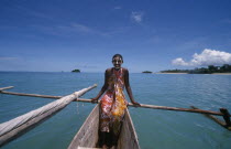 Young girl on a pirogue canoe wearing a colourful sarong and with her face painted.  Turquoise sea.