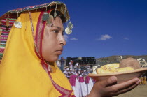 Woman in traditional headress carrying an offering of food during Inti Raymi.  Head and shoulders shot  profile to the right.