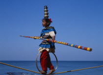 Young girl walks the tightrope while balancing silver pots on her head  blue sky in background