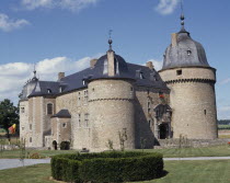 Medieval Chateau a stone building with a black roof and circular boxed hedge in the foreground
