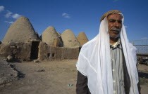 Old man stands outside beehive mud houses