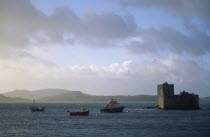 Scotland, Outer Hebrides, Isle of Barra, Castle Bay, Kisimul Castle overlooking sea and moored fishing boats.