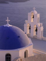 Thira detail of blue and white church dome and bell tower at dusk with the sea below