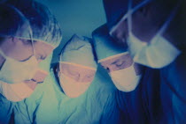 Operating theatre with five medical staff wearing surgical masks looking down towards patient