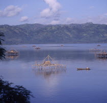 Bamboo fishing platforms in the sea with a man in a canoe rowing towards one