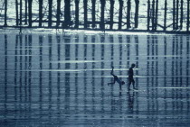 Two boys playing on the beach at low tide beside the pier