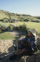 Basotho Cultural Village  local man playing an instument called a Sekoankula  hills and huts in background.