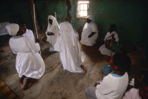 Zulu Zionists women wearing white kneeling on the earth ground inside a house praying
