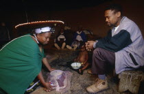 Zulu woman kneeling to give tea to her seated husband.