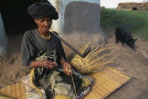 Elderly Xhosa woman making basket and smoking long pipe.