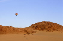 Hot air ballooning above rocky outcrop over sand dunes