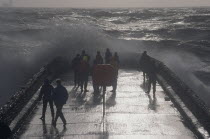 Waves crashing over a groyne with people on it