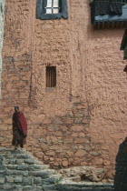 Monk standing on steps in front of peach coloured painted wall