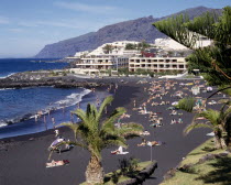 Playa de la Arena near Los Gigantes with sunbathers on black sandy beach and apartments in the distance