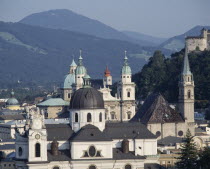 Town rooftops with domed spires a hilltop fortress and wooded hills behind