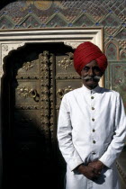 Palace guard dressed in white and wearing a red turban standing by ornate doorway