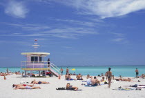 Sunbathers on the beach by a colourful lifeguard hut