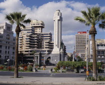 Santa Cruz. Plaza de Espana and Civil War Monument of grey stone and a tall cross with city skyline behind