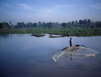 Praya  man fishing from outrigger canoe using circular casting net  lake weeds & trees behind J6599