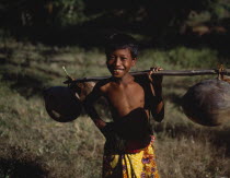 Mawon near Kuta a young boy in floral sarong holding pole of dried coconuts across his shoulder