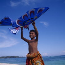 Young boy in red floral sarong holds up a blue eagle shaped kite