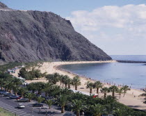 Las Teresitas. Long sandy bay beneath black cliffs and palm lined promenade with parked cars
