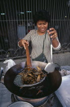 Woman cooking insects in a wok at a market stall