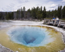 People looking into Morning Glory hot pool in the National Park.  Ochre and turquoise rock