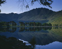 Buttermere.  Rugged hills and trees with mirror reflection in lake.