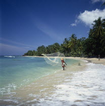 Fisherman casting fishing net into sea from the surf on a coconut palm tree lined sandy beach