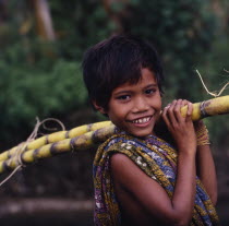 Smiling boy with a sarong over his shoulder carrying sugarcane
