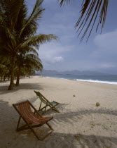 Beach golden sand two empty deckchairs palm trees distant hills