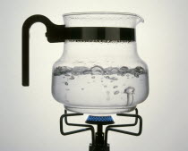 Steam rising from water boiling in a glass jar on a gas ring