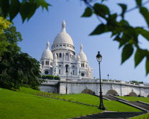 Sacre Coeur.  Exterior against blue sky partly framed by tree branches.