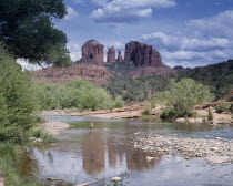 Cathedral Rock in Oak Creek Canyon. View across river towards wind eroded rock features with a boy wading in the water.