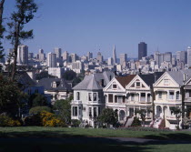 Alamo Square with city skyline beyond a row of timber town houses with steps leading up to doorways